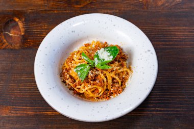 Zengin et sosu ve taze fesleğenle kaplanmış bir tabak spagetti kırsal ahşap bir masaya yerleştirilir. Yemek rendelenmiş peynirle süslenir. Yemekleri doyurucu bir yemeğe davet edilir..
