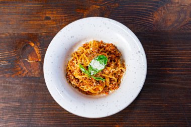 Bol et soslu, taze fesleğenle süslenmiş cömert bir spagetti. Tabak, kırsal ahşap bir masanın üzerinde benekli beyaz bir tabakta sunuluyor..