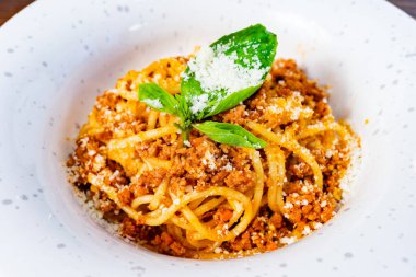 Lezzetli bir makarna tabağında taze fesleğen yaprakları ve bir tutam peynirle süslenmiş zengin bir et sosu bulunur. Bu yemek öğle yemeği ya da sıcak bir restoranda akşam yemeği için mükemmel..