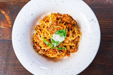 Bol et soslu ve taze fesleğenle süslenmiş lezzetli bir spagetti. Bu yemek sade beyaz bir tabakta sade bir tahta masaya sunuluyor..