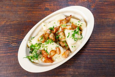 Kızarmış pastırma ve taze otlarla kaplı bir tabak ev yapımı hamur köftesi köy ahşabı bir masada oturur ve geleneksel mutfağın konforlu yemeklerini sergiler..