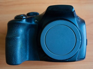 Siyah bir kamera ahşap bir yüzeye yerleştiriliyor ve üst manzarayı gösteriyor. Mercek kapağı açık, kullanılmadığını gösteriyor. Bu resim kameranın dizaynını ve dokusunu vurgular.