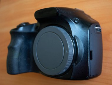 Ahşap bir yüzeye yerleştirilmiş bir kamera kullanıma hazır. Mercek kapağı yerinde, tasarımı ve detaylarıyla sergileniyor. Ayarlar fotoğrafçılığa odaklanmayı vurgular.