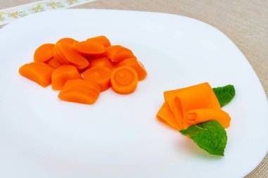 Parlak renkli havuç dilimleri, dekoratif havuç kurdelesi ve taze nane yapraklarıyla beyaz bir tabakta ustaca düzenlenir. Sunuma zarafet katar..