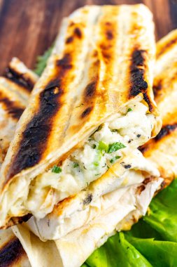 Izgara ambalajlar ahşap bir tahtaya istiflenmiş, içinde erimiş peynir ve taze bitkiler sergileniyor. Sargılar hafif kömürleşmiş, iştah açıcı görünüşlerine katkı sağlıyor..