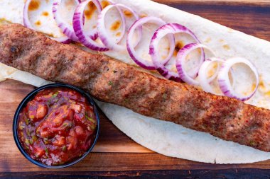 Lezzetli bir kebap taze soğan dilimleriyle süslenmiş ve yanında bir kase salsa sosuyla birlikte bir parça düz ekmeğin üzerine yerleştirilir. Bu iştah açıcı yemek canlı tatlar sergiliyor..
