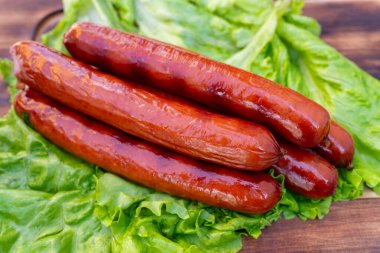 Beş ızgara sosis kıvırcık marul yapraklarından bir yatakta dinleniyor, güneşli bir öğleden sonra bir yaz toplantısında servis edilmeye hazır. Canlı renkler iştah açıcı görünümü arttırır..