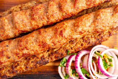 Lezzetli ızgara kebaplar sade ahşap bir tabakta sunulur. Taze dilimlenmiş soğan ve otlar taze bir dokunuş ekleyerek yemeğin cazibesini ve tadını arttırır..