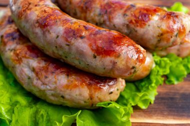 Sulu sosisler, açık hava barbekü partisinde servis edilmek üzere gevrek marul yatağında dinlenen altın-kahverengiyi gözler önüne seren mükemmel ızgarada kızartılıyor..