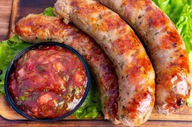 Sulu, ızgara sosisler taze salsa sosunun yanında, kıvırcık bir kıvırcık kıvırcık kıvırcık kıvırcık salatanın üzerinde duruyor. Bu yemek lezzetli lezzetler ve dokular sunar..