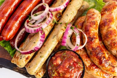 Taze soğan dilimleriyle süslenmiş baharatlı ve hafif sosisler de dahil olmak üzere lezzetli bir ızgara sosis, ahşap tabakta bir kase salsa ile servis edilir..