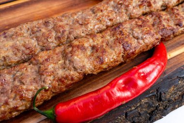 Sulu kebaplar ahşap bir yüzeyde dinlenir ve yanında canlı kırmızı biber vardır. Izgara izleri yeni bir pişirme sürecini işaret ediyor. Lezzetli dokuyu ve aromayı vurguluyor..