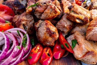 Sulu ızgara et parçaları canlı kırmızı soğanlar, taze domatesler ve baharatlı biberlerin yanında düzenlenir ve yaz kutlaması için mükemmel bir davet tabağı oluşturur..