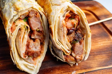 Izgara et ve karides katmanlarıyla dolu tuzlu ambalajlar sergileniyor. Tahta bir tahtanın üzerinde hareketli bir yiyecek pazarı atmosferini yansıtıyorlar..