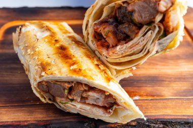 İki ızgara et ve canlı sebzelerle dolu ambalaj ahşap bir yüzey üzerinde dinleniyor. Altın-kahverengimsi dış görünüşü mükemmelce yanmış, iştah açıcı katmanları vurguluyor..