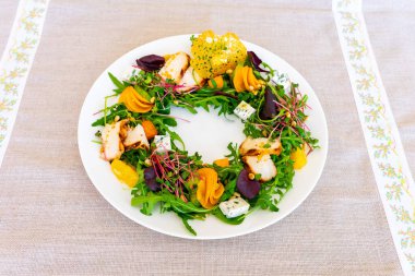 Çok güzel düzenlenmiş bir salata, ızgara tavuk dilimleri, parlak kızarmış sebzeler ve taze sebzeler, basit bir masa örtüsüne karşı dizilmiş. Tabak sanatsal sunumu gösterir.