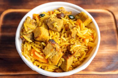 Bir kase dolusu aromatik tavuk biryani vitrinleri taze tavuk parçaları, kokulu pirinç ve baharatlar. Canlı, ahşap bir yüzeyde sanatsal bir şekilde sergileniyor, iştahı kabartıyor..