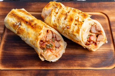 Taze et ve taze sebzelerle dolu ahşap bir tahtanın üzerinde iki altın sarısı rulo hamur işi duruyor. Susam tohumlarıyla süslenmişler. Lezzetli ve iştah açıcı bir yemek sergiliyorlar..