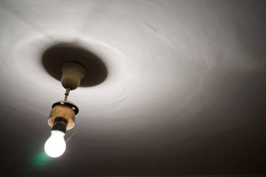 Tavandan sarkan tek bir ampul küçük bir alanı aydınlatıyor. Ampul dokulu tavana yumuşak gölgeler bırakır ve uzayda sakinleştirici bir atmosfer yaratır..