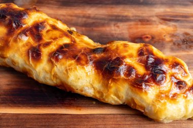 Çıtır çıtır, altın-kahverengi kabuklu yeni pişmiş bir hamur işi ahşap bir yüzeye yerleştirilir. Yumuşak dokusu ve cazip görünüşüyle herkesi bir ısırık almaya davet eder..