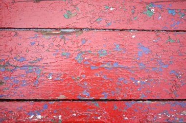 Kırsal kırmızı ahşap bir yüzeye yakın çekim. Kapsamlı soyulan boyaları gösteriyor. Çok renkli benekler yıpranmış dokuya karakter ekler, elementlere yıllarca maruz kalmanın altını çizer.