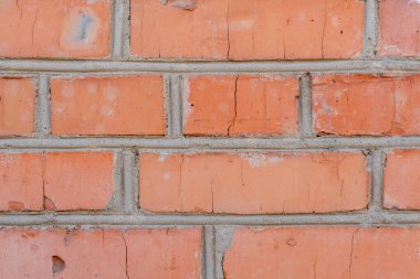 Eski bir kırmızı tuğla duvarda gözle görülür çatlaklar ve yıpranmış havan topları görülüyor. Doku ve renk, duvarın geçmişini ve zamanla elementlere maruz kaldığını gösteriyor..