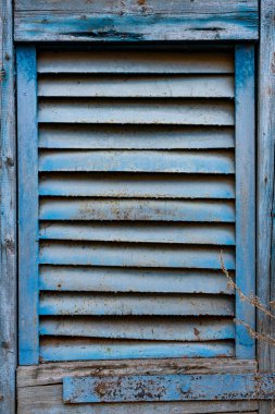 Eski mavi panjurlar, hafif yıpranmış ve yıpranmış, kırsal bir binaya kapatılmışlar. Kabuk soyma boya ve ahşap doku, sakin bir ortamda elementlere yıllarca maruz kaldığını gösteriyor..