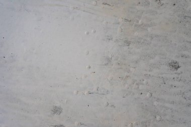 Açık renkli kumlu bir yüzey, kenar mahalleleri işaret eden belirsiz, belirsiz hayvan izleri gösterir. Ayar, açık gün ışığı altında doğal bir ortam izlenimi veriyor..