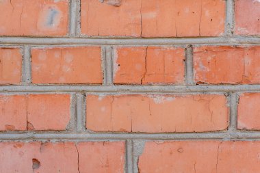 Eski bir kırmızı tuğla duvarda gözle görülür çatlaklar ve yıpranmış havan topları görülüyor. Doku ve renk, duvarın geçmişini ve zamanla elementlere maruz kaldığını gösteriyor..