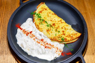 Taze yapılmış bir omlet, yanında zengin, kremalı bir sos ile siyah bir tabakta oturur. Bitkiler ve baharatlarla süslenmiş bu yemek sağlıklı bir yemek için mükemmel.