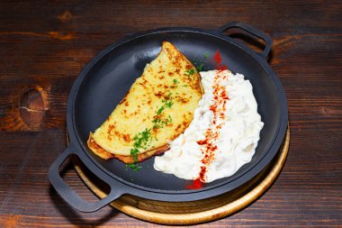 Güzel kaplanmış bir omlet, bol miktarda kremalı sosun yanında, otlar ve baharatlarla süslenmiş, kırsal bir ortamda sıcak ve davetkar bir atmosferi ön plana çıkarıyor.