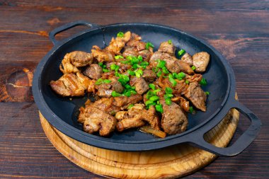 Sulu et parçaları mükemmel pişirilir ve canlı yeşil soğanlarla süslenir. Tabak, siyah dökme demir bir tavada sunuluyor, kırsal bir yemek deneyimini vurguluyor.