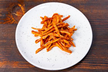 Canlı bir portakal sosu ile kaplanmış gevrek domuz kulakları kırsal ahşap bir zemine karşı beyaz bir tabakta servis edilir ve iştah açıcı bir sunum oluşturur..