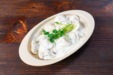 Taze hazırlanmış hamur köfteleri kremalı bir sos içinde garnitür otlarla servis edilir, kırsal ahşap bir masanın üzerinde bej bir tabakta dinlenir. Sağlıklı bir yemek için mükemmel..