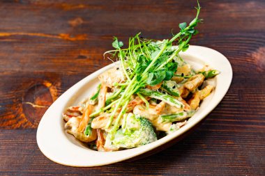 Lezzetli bir makarna tabağında kremalı sosla kaplanmış brokoli ve havuç gibi canlı sebzeler bulunur. Taze otlar yemeği süsleyip sunumunu ve tadını artırır..