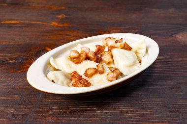 Üstünde altın, çıtır çıtır domuz eti olan bir tabak hamur köftesi ahşap bir masada oturur. Dekorasyon, sıcak, kırsal bir yemek deneyimini ön plana çıkarıyor, doyurucu bir yemek için mükemmel..