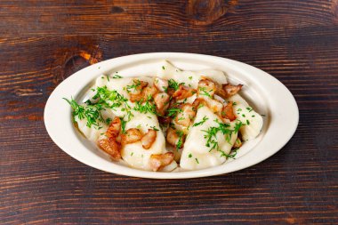 Kıtır pastırma ve taze otlarla kaplı bir tabak yumuşak hamur köftesi kırsal bir ahşap masada duruyor. Sıcak yemek sıcak bir yemek deneyimine davetiye çıkarır..