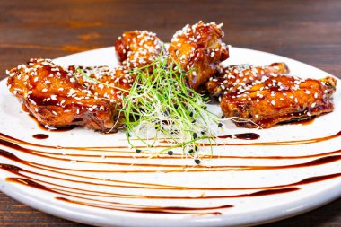 Zengin bir sosla kaplanmış ve susam tohumları ve taze yeşilliklerle kaplı lezzetli tavuk kanatları. Bu yemek zevki paylaşmak ya da tek başına eğlenmek için mükemmel..