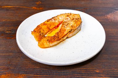 Güzel pişirilmiş bir somon fileto sade beyaz bir tabakta oturur, altın-kahverengi yüzeyini sergiler ve hafif süslenir, bir gurme yemeği sunumu için uygundur..