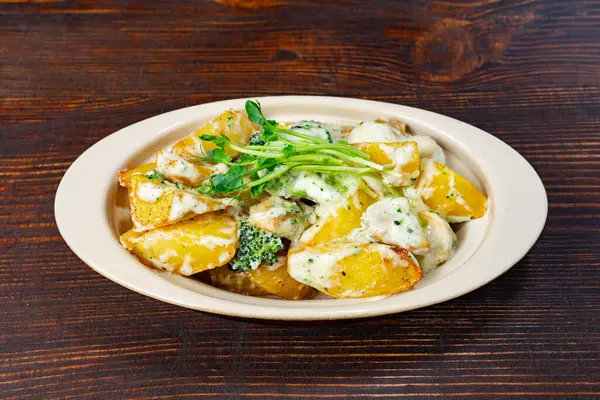 Kremalı sosla kaplanmış, yeşil otlarla süslenmiş ve yeşil otlarla süslenmiş altın fırında patates, tarafsız bir tabakta sade bir ahşap masaya servis ediliyor..