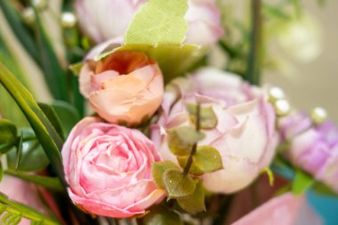 Canlı bir buket, canlı yeşilliğin yanında yumuşak pembe ve şeftali gülleri barındırır. Düzenleme zarif yaprakları ve dekoratif unsurları içeriyor, davetkar bir atmosfer yaratıyor..