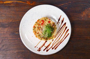 Çok güzel düzenlenmiş bir orzo makarna tabağı toprak tonları ve canlı sebzeler içerir. Taze yeşil lahanalarla süslenmiş, modern tabakta aşçılık sanatını sergiliyor..