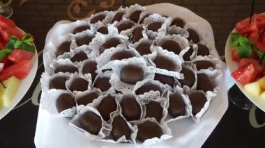 Çeşitli el yapımı çikolatalı şekerlemeler, canlı bir toplantıda taze meyvelerle çevrili bir tabakta güzelce düzenlenerek, şenlikli bir atmosfer yaratılıyor.