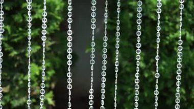 Berrak damlacıklar yemyeşil ortamda sakin ve sakinleştirici bir atmosfer yaratan yemyeşil bir bahçedeki narin cam tellerden akarken güneş ışığını yansıtırlar..