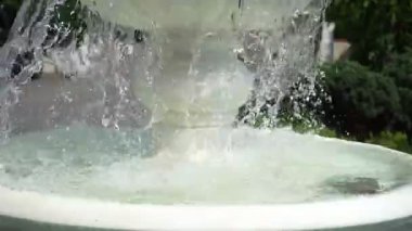 Su, yemyeşil bir bahçedeki güzel bir çeşmeden zarif bir şekilde süzülür. Güneş ışığı yüzeyde parlıyor, canlı yeşillikler arasında barışçıl bir ortam yaratıyor.