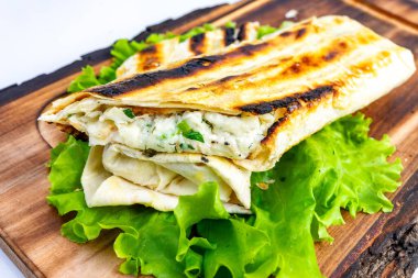 Bu tabakta krem peynirle doldurulmuş altın ızgara ekmek dürümü ve taze otlar var. Canlı yeşil marul yatağında dinleniyor, tadını çıkarmaya hazır..