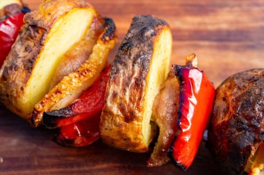 Izgara sebze ve etin yer aldığı renkli şişler ahşap bir yüzey üzerinde sunuluyor. Canlı biberler ve çıtır çıtır kenarlar açık havada yapılan lezzetli hazırlığın altını çiziyor..