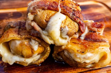 Üç lezzetli pastırmaya sarılmış mantar kapağı eritilmiş peynirle dolu ahşap bir tahtanın üzerinde oturur. Yemek, iştah açıcılar ya da sağlıklı atıştırmalıklar için mükemmel bir karışım sunuyor..