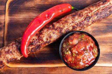 İçten bir kebap ahşap bir tahtanın üzerinde taze kırmızı biberle tamamlanmış canlı salsa sosunun yanında oturur. Yemekler lezzetli dokular ve tatlar sergiliyor. Yemek için ideal..