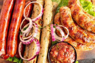 Dilimlenmiş soğanla süslenmiş ve yanında taze salsa sosuyla servis edilen çeşitli ızgara sosislerden oluşan canlı bir gösteri. Bu renkli tabakta açık hava buluşmaları için mükemmel tatlar var..